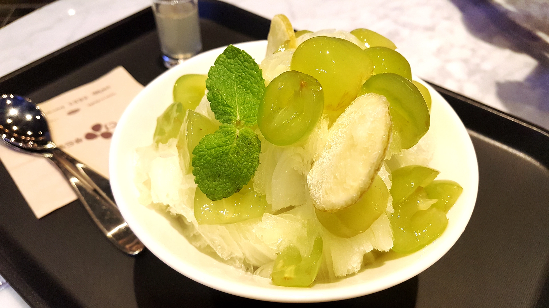 A bowl of bingsu with an assortment of green grapes and mint on top of it